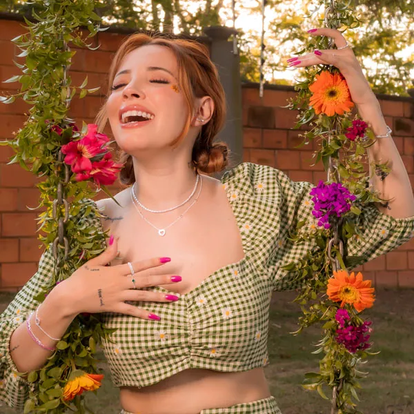 A digital influencer Taciele Alcolea sentada em um balanço cheio de flores coloridas 